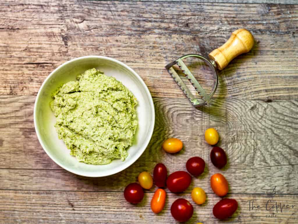 bowl of garlic scape filling with ravioli press and cherry tomatoes
