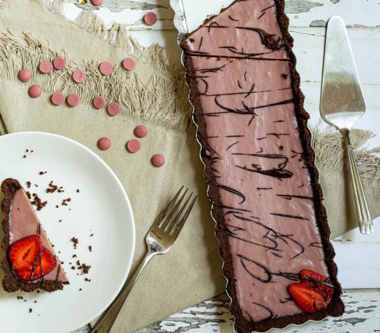 Plate with a slice of tart next to ruby chocolate tart in a pan
