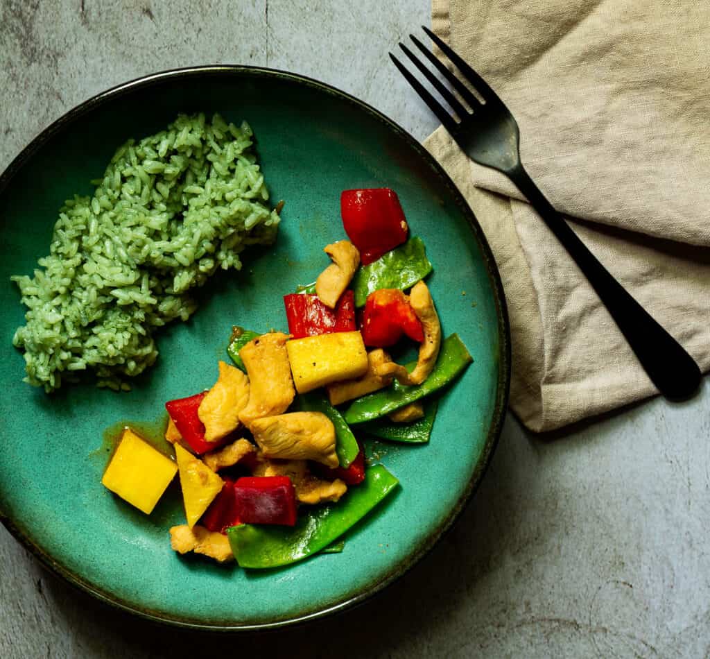 chicken pineapple stir fry in a green bowl with bamboo rice with a napkin and fork