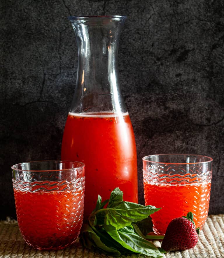two glasses of stgrawberry basil lemonade with a pitcher