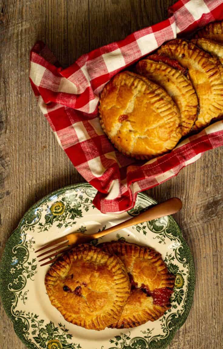 Hand pies on a plate next to hand pies in a dish wrapped in a red and white checked towel