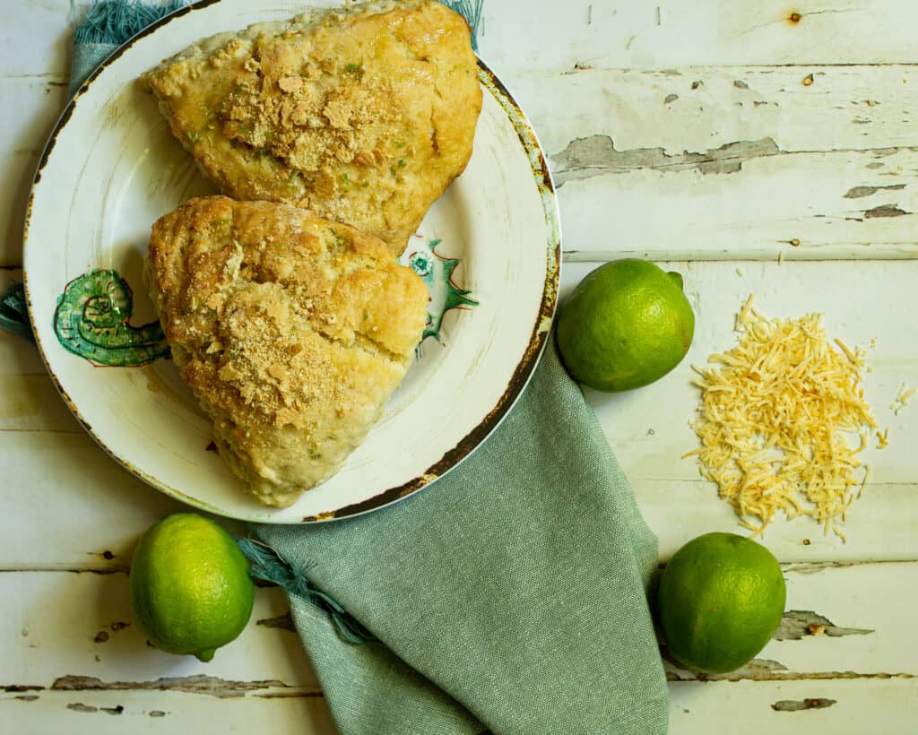 two scones on a white plate with limes and toasted coconut