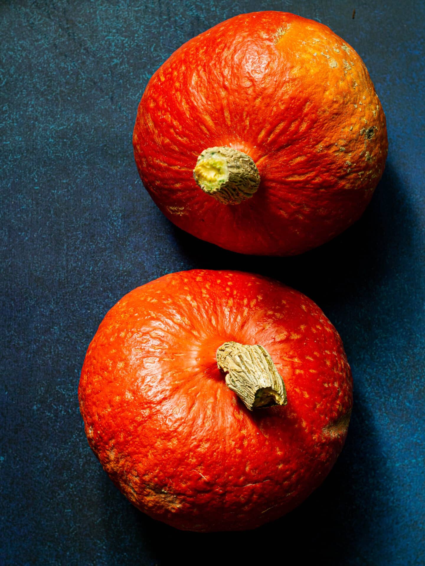 two whole red kuri squash on a blue background