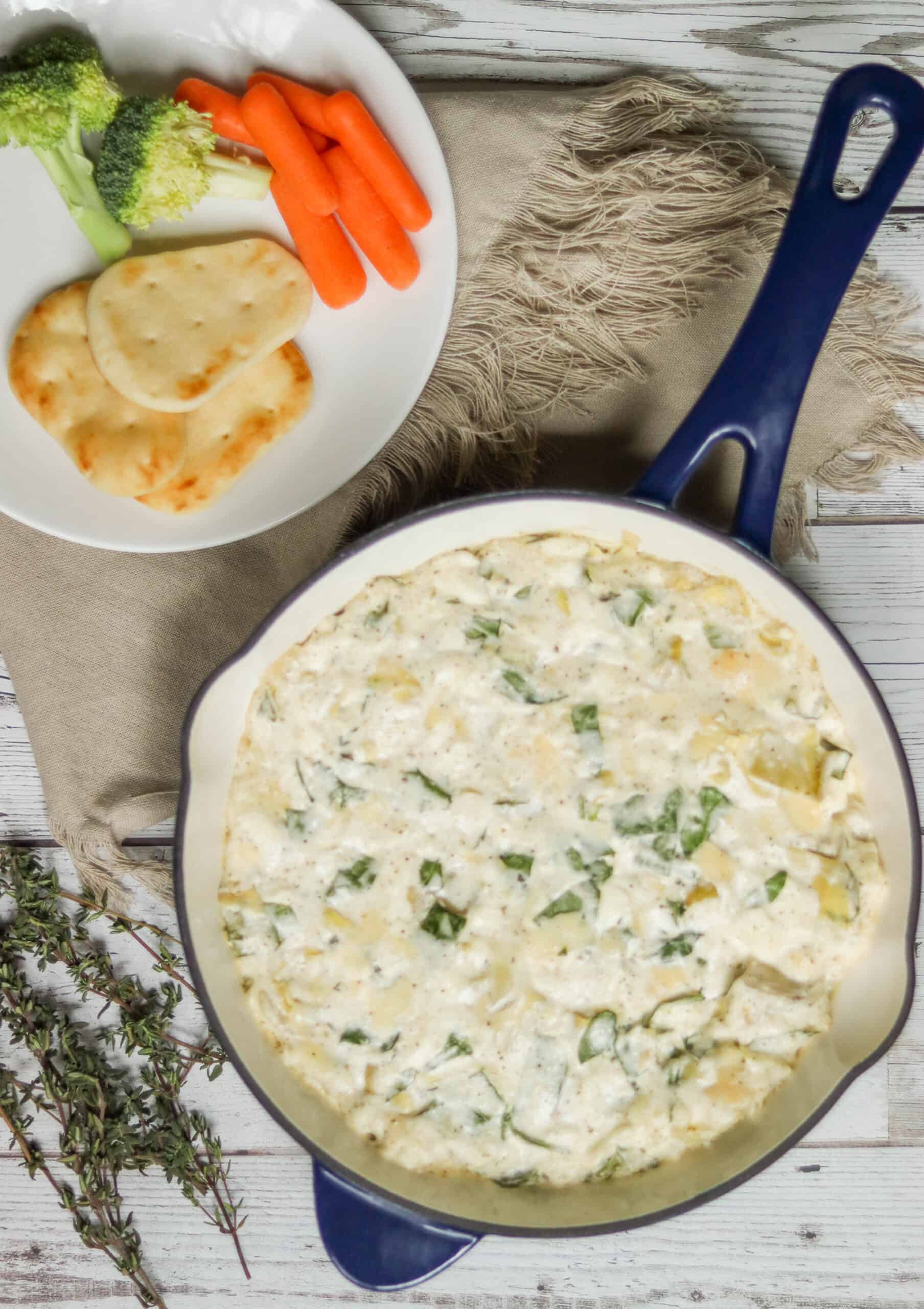 Artichoke spinach dip in a skillet with vegetables and bread