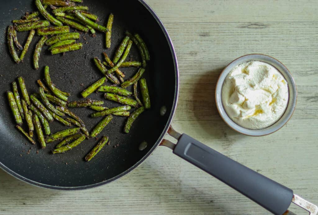 pan of sauteed garlic scapes next to a bowl of ricotta cheese