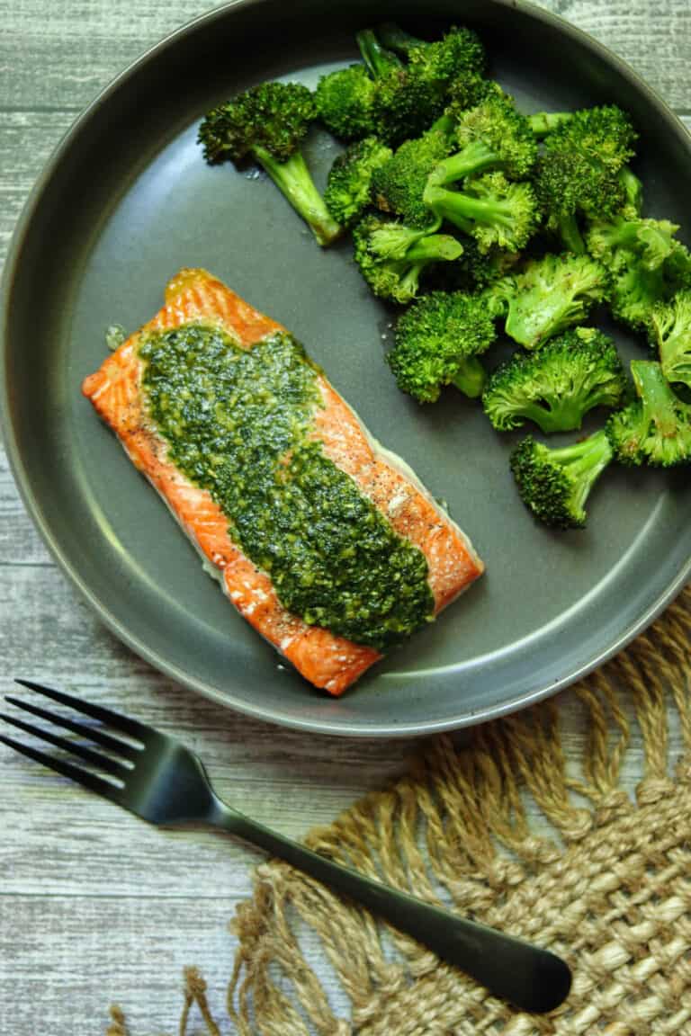 salmon with pesto butter and broccoli next to a fork.