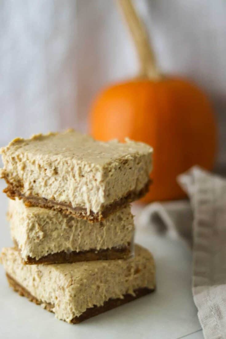 Stack of three pumpkin cheesecake bars with a napkin.