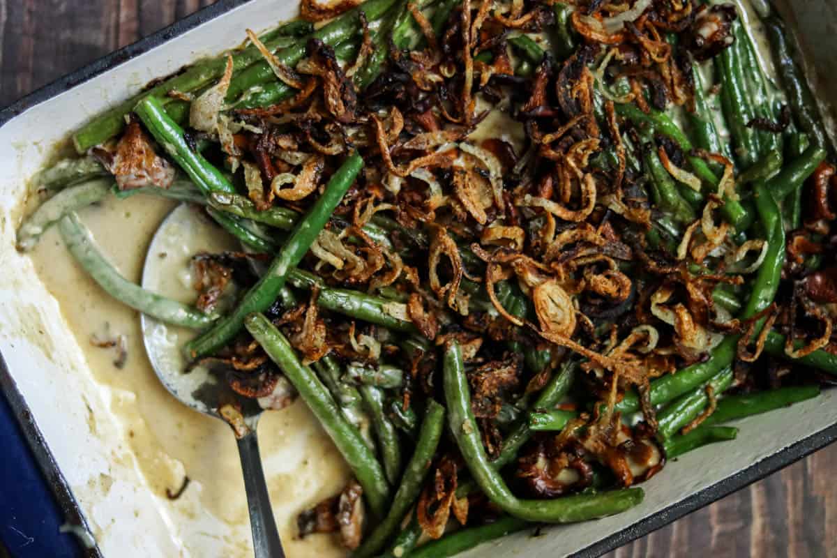 close up photo of green bean and chanterelle mushroom casserole in a blue dish with a spoon.