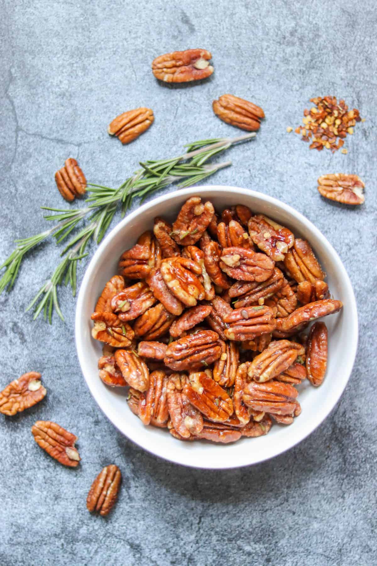 candied pecans in a bowl with fresh rosemary and red pepper flake