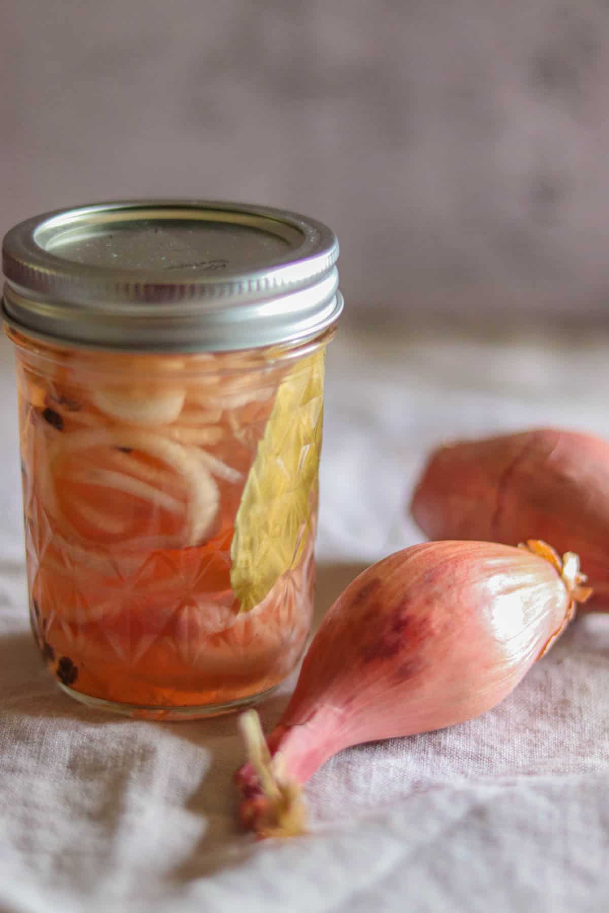 jar of pickled shallots next to a shallot.