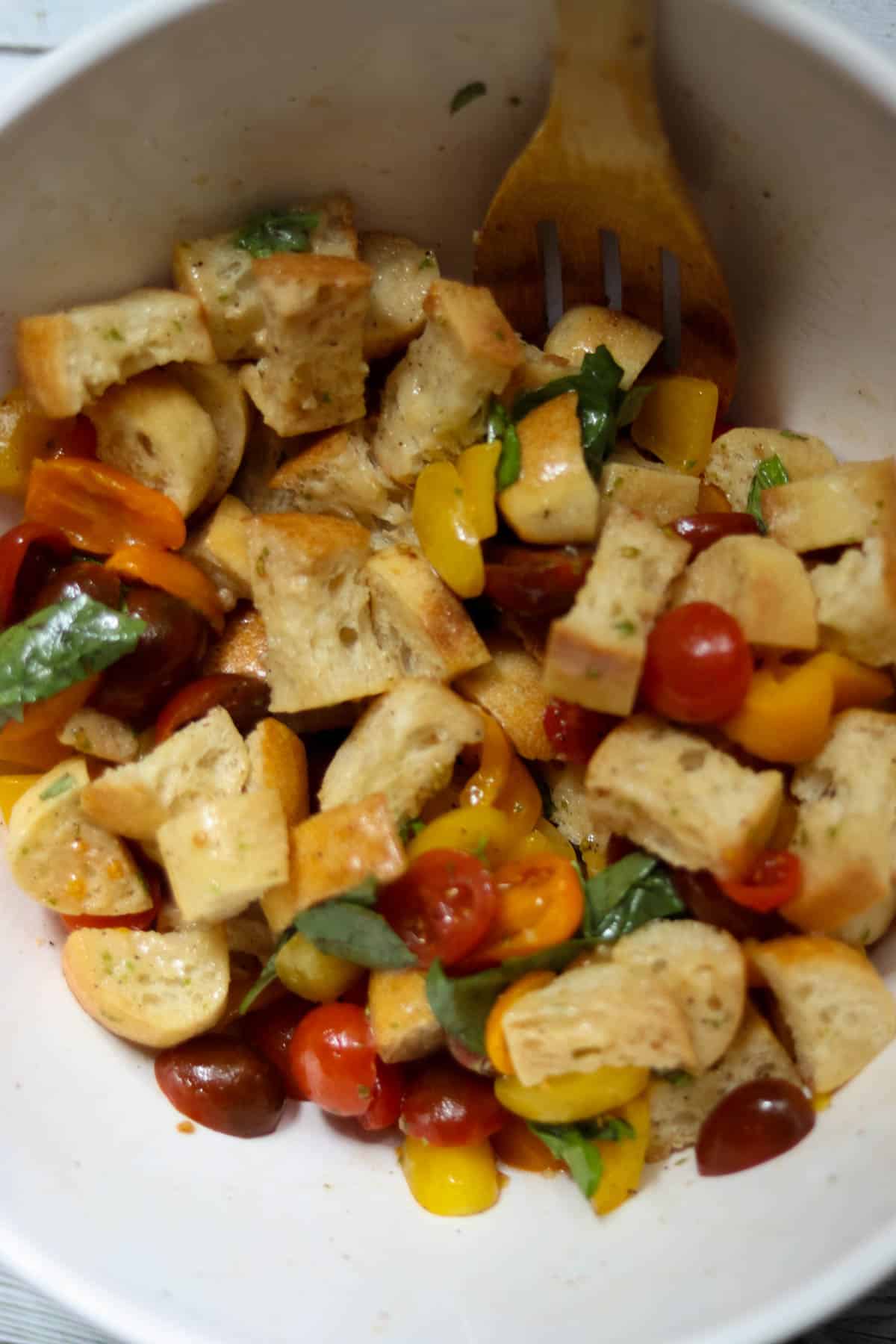 Panzanella Toscana in a bowl being stirred with a wooden spoon.