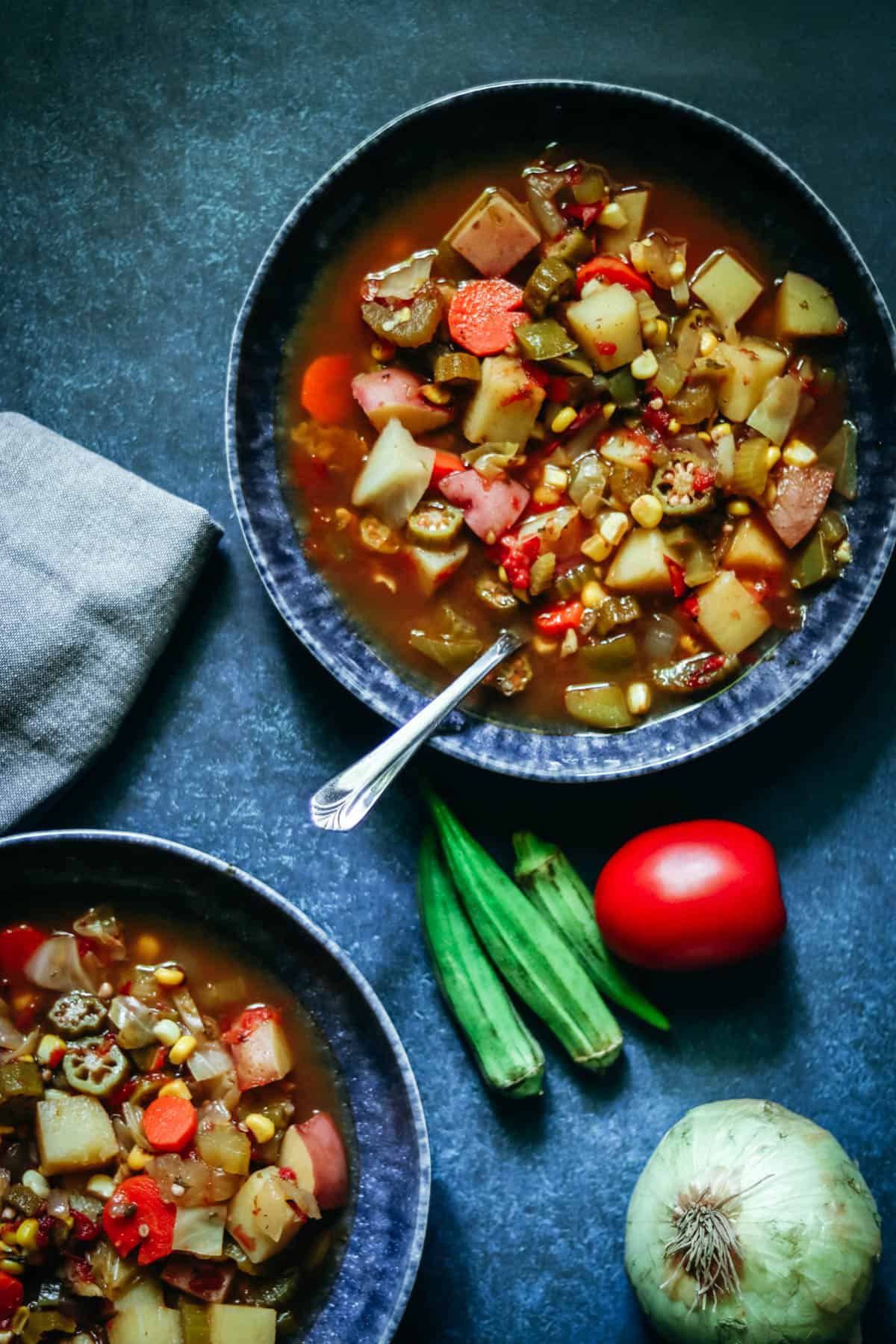 two blue bowls with vegetables soup and a spoon.