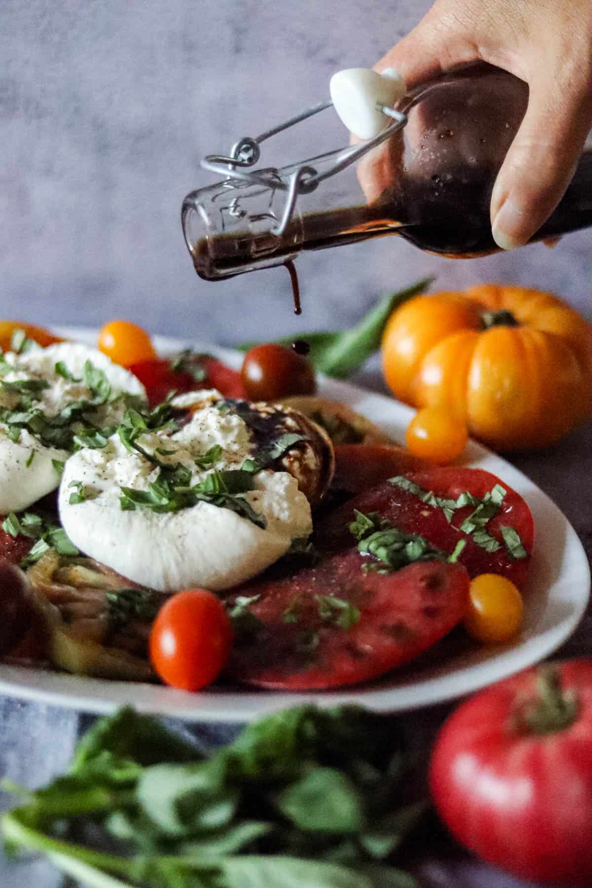Pouring balsamic vinegar over the top of a burrata caprese salad.