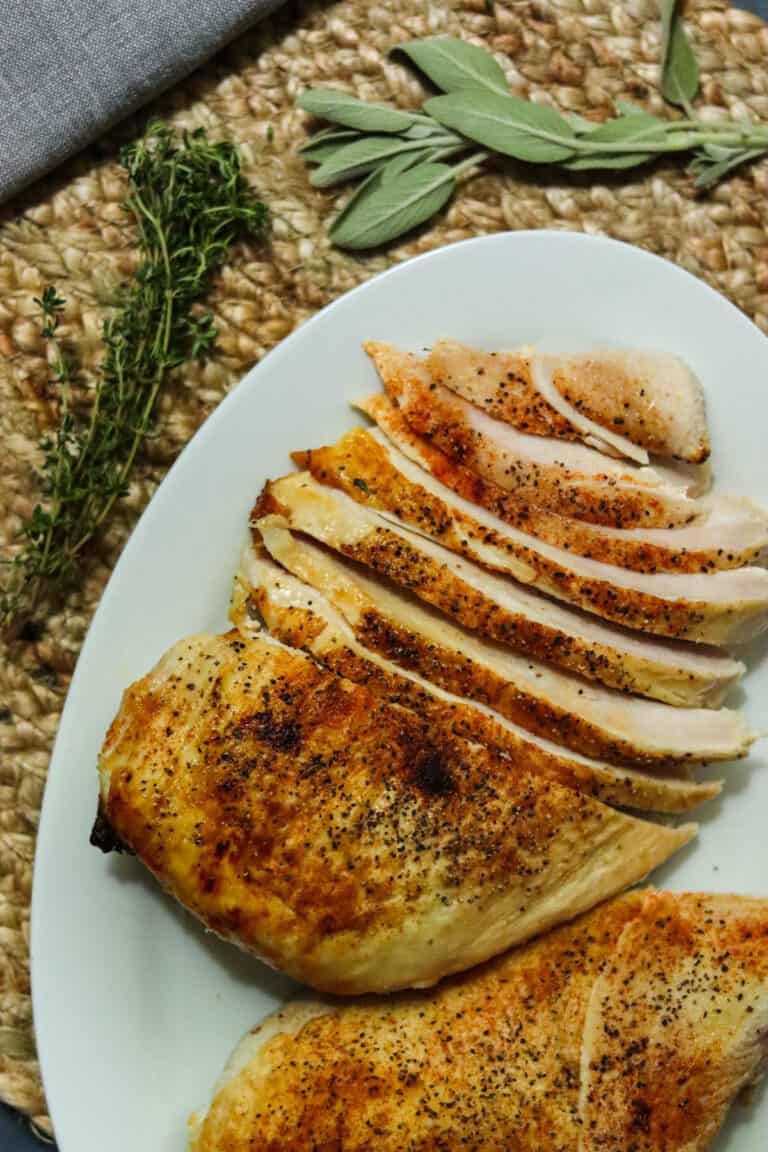 Sliced roasted turkey breast on a plate with fresh herbs.