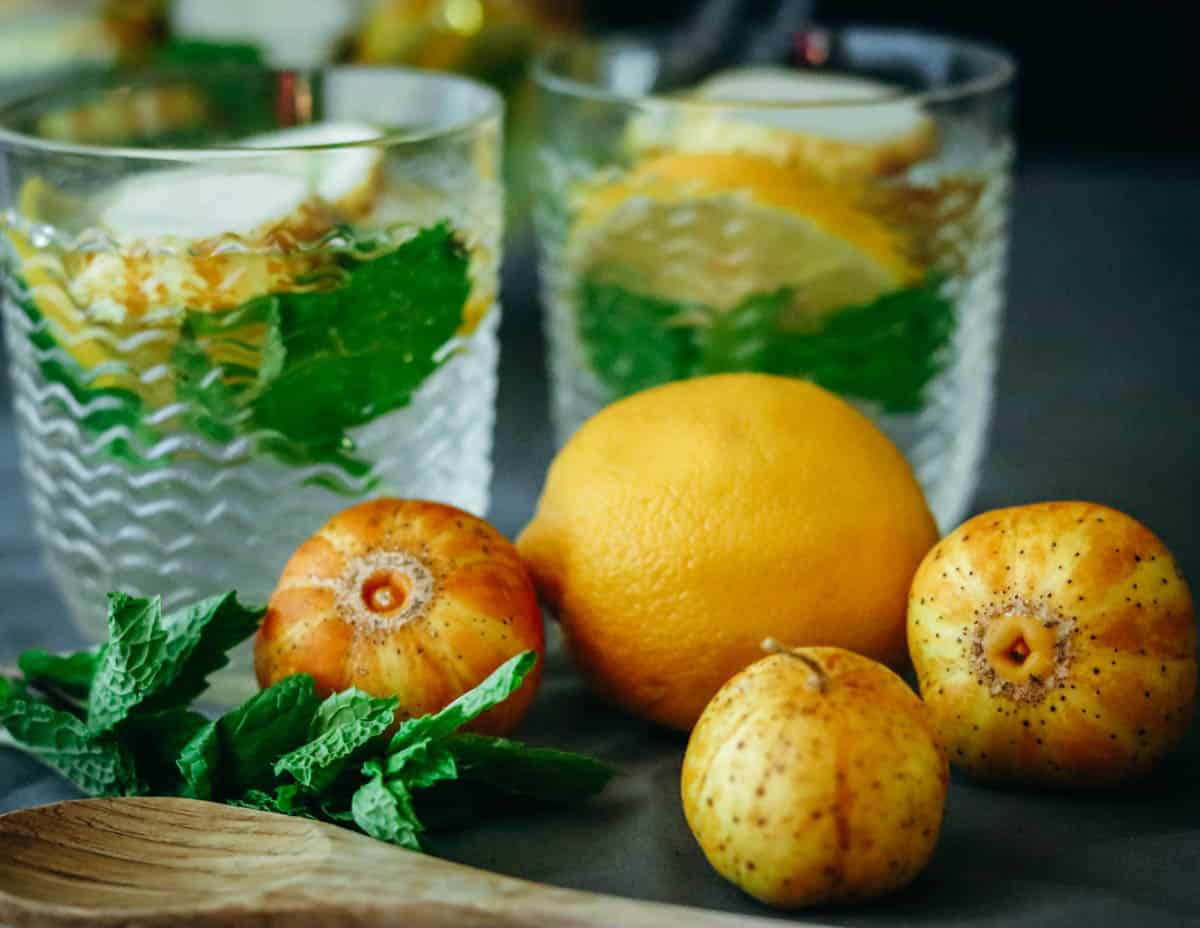 Three lemon cucumbers with a lemon and glasses of water with cucumber and lemon in them.