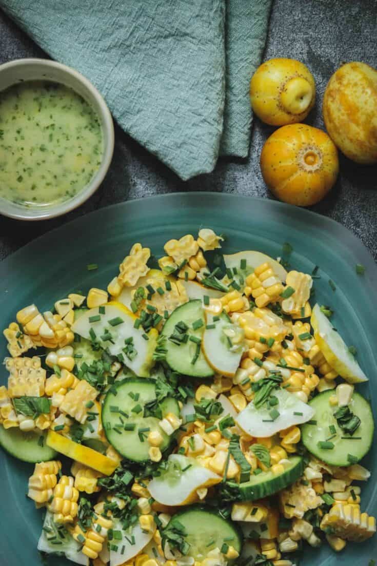 Salad of chopped lemon cucumber, corn, and herbs next to whole lemon cucumbers.