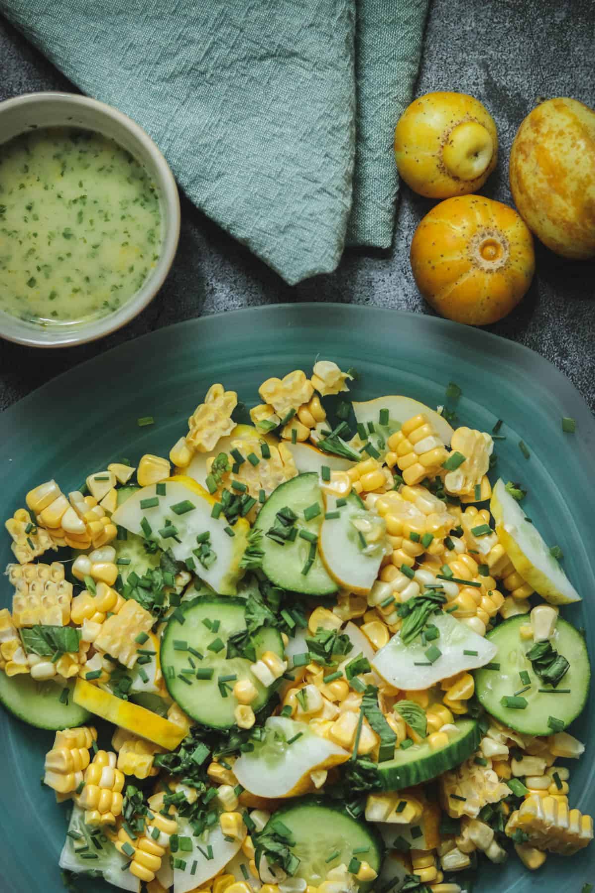 Salad of chopped lemon cucumber, corn, and herbs next to whole lemon cucumbers.