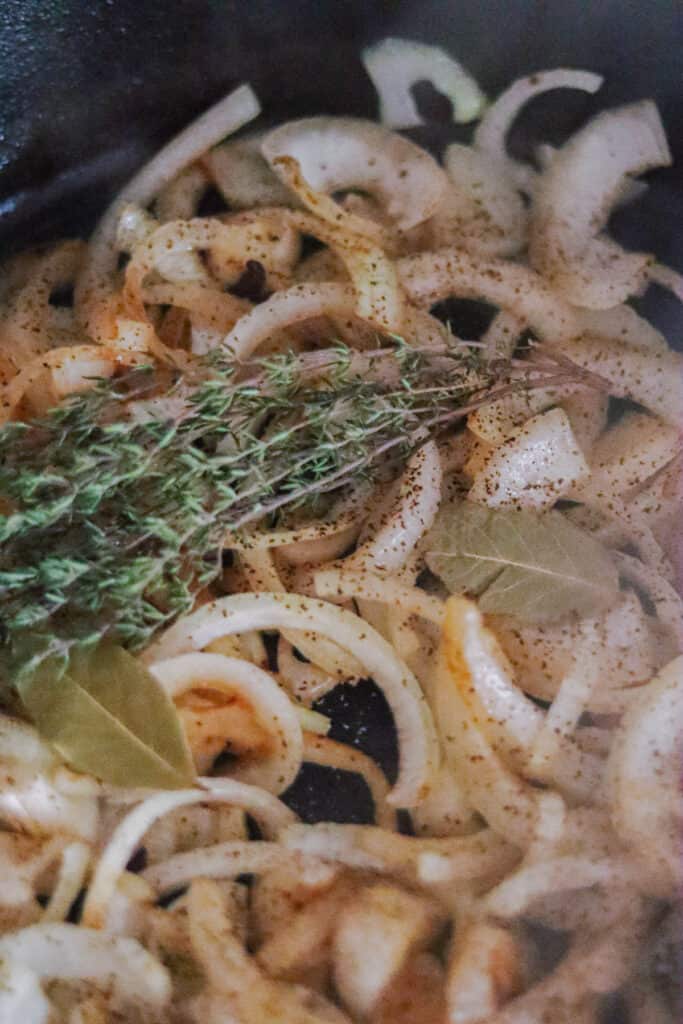 Sliced onions in a skillet with bay leaves and fresh thyme.
