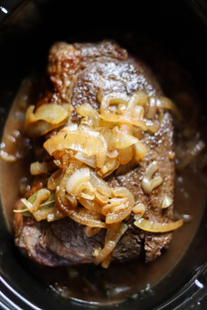 Onions poured on top of the roast in the slow cooker.