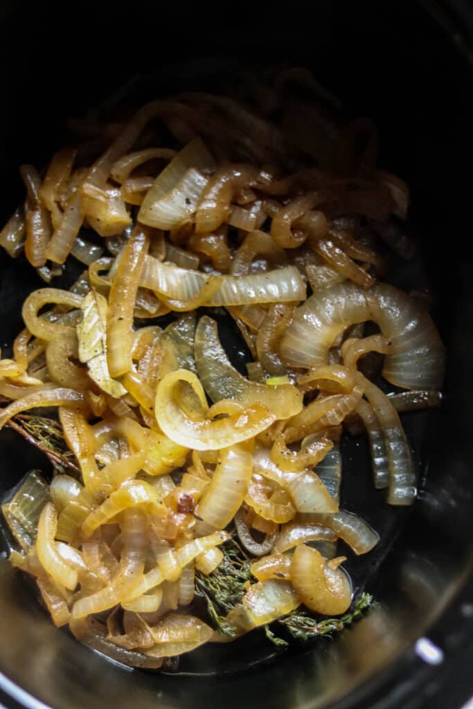 Sliced onions in the bottom of a slow cooker.