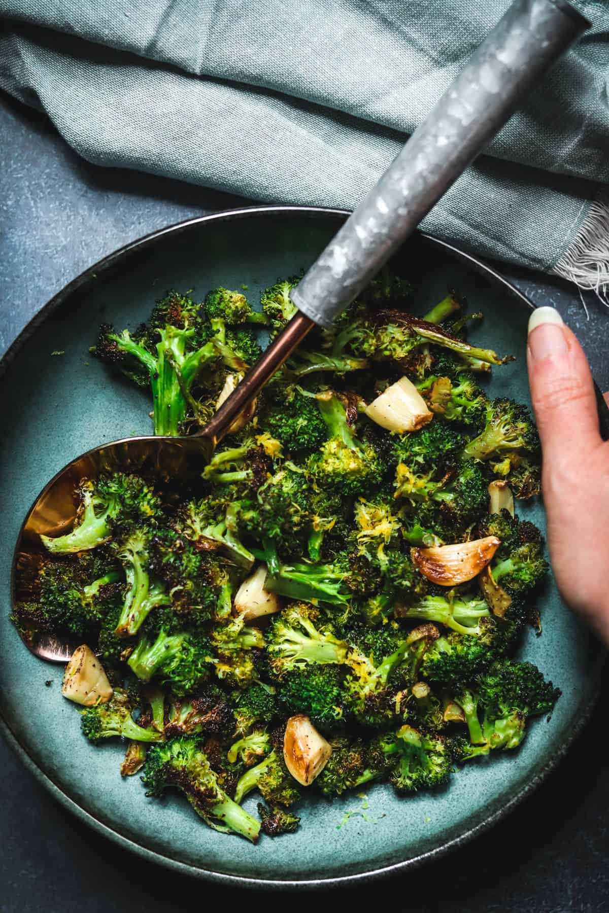 Hand holding a bowl of charred broccoli.