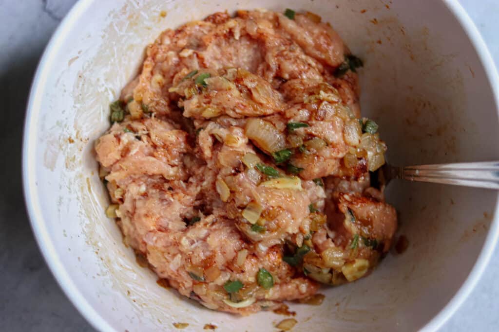 Onion mixture and seasonings being stirred into the ground chicken.