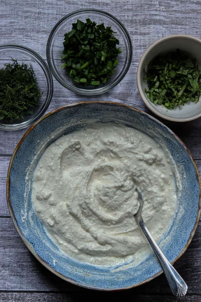 Bowl of dip base with dishes of fresh herbs.