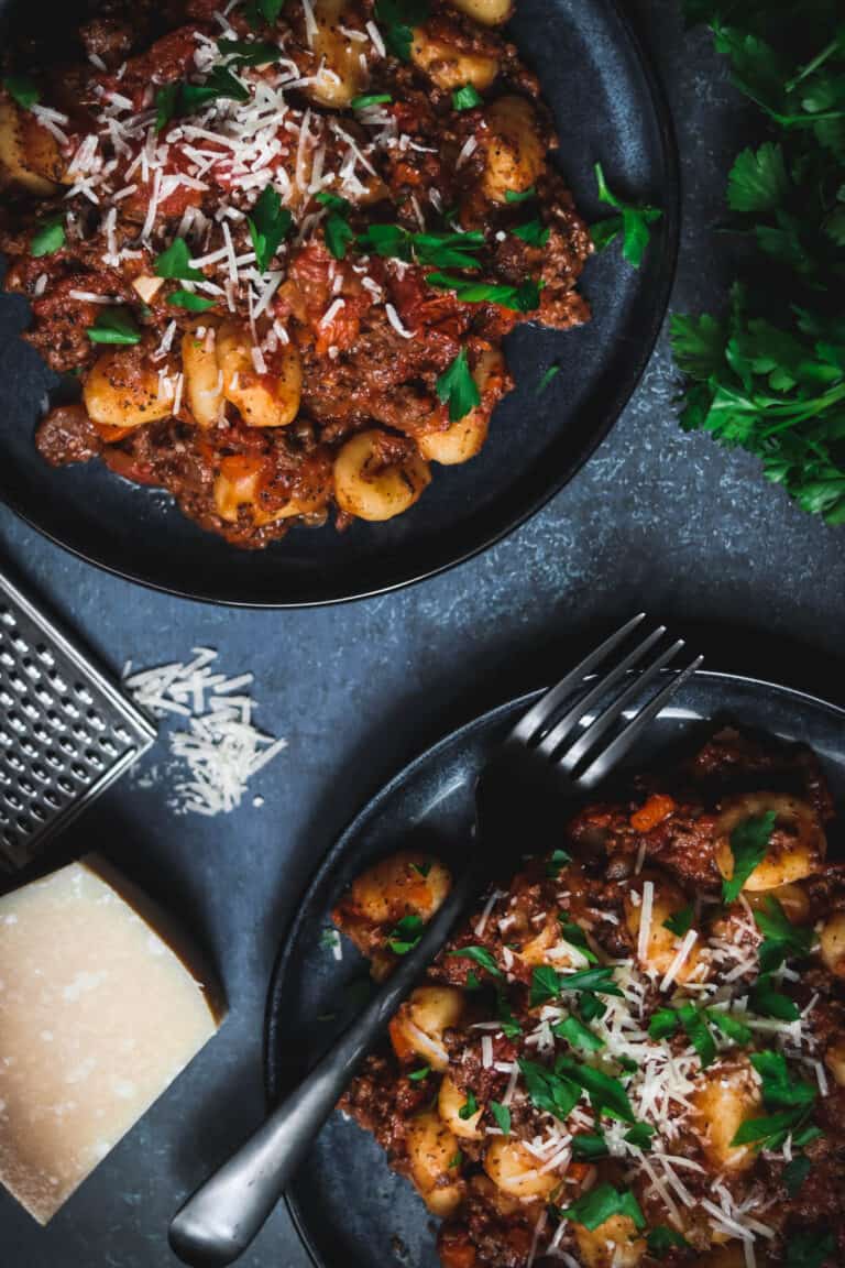Two plates of gnocchi with bolognese sauce.