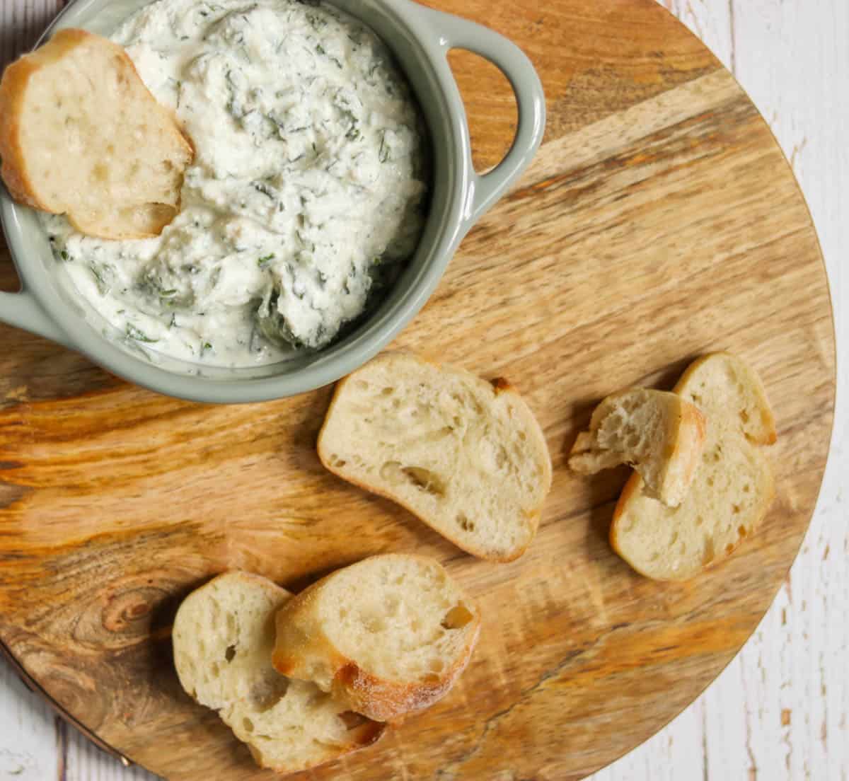 Dish of dip on a wooden serving board with bread.