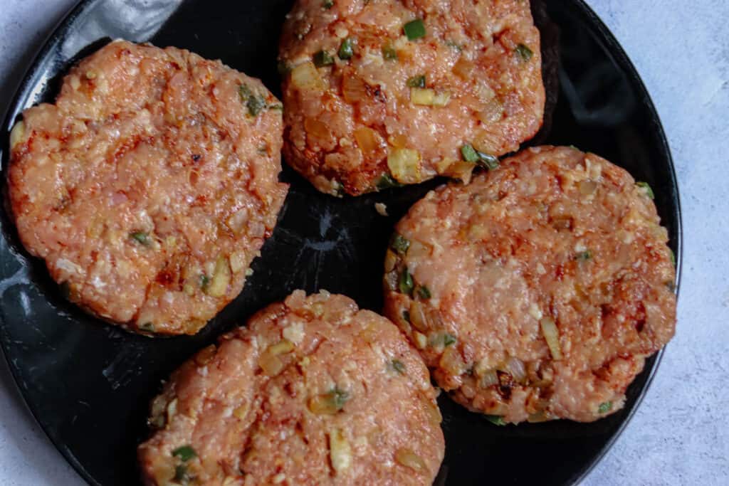 Four chicken burger patties on a plate.