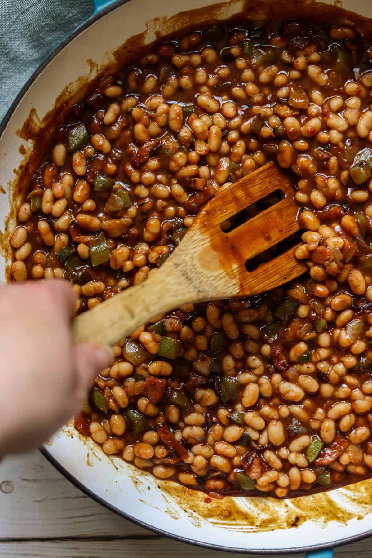 Jalapeno Bacon Baked Beans being stirred by a wooden spatula.