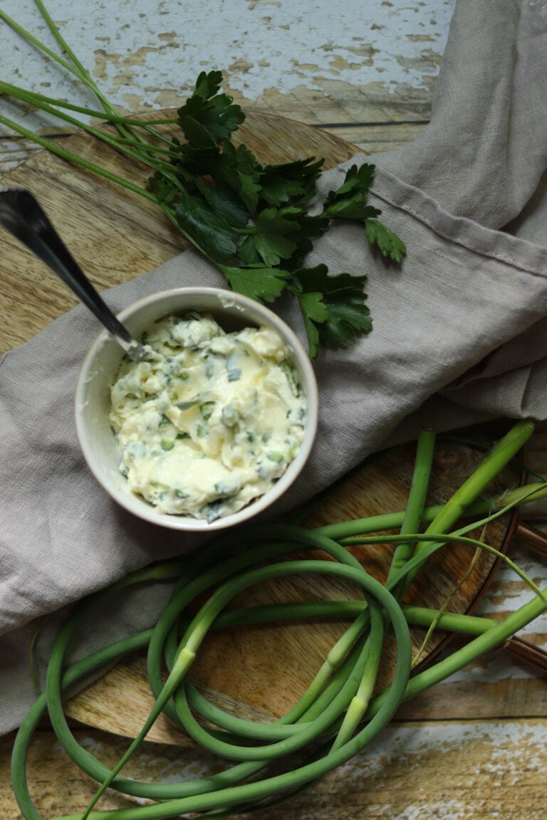 Butter with garlic scapes on a wood background with a spoon.