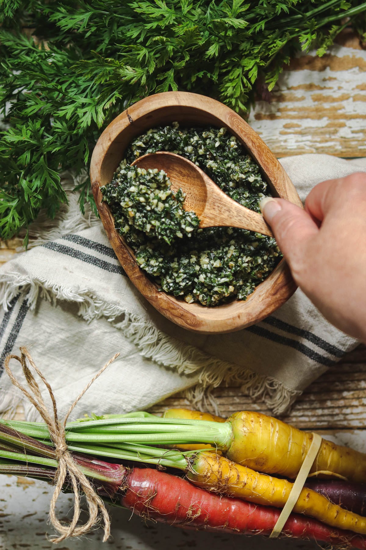 Carrot top pesto in a wooden bowl being scooped with a wooden spoon.