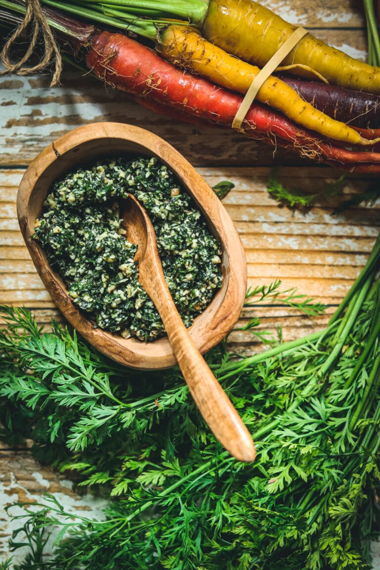 Pesto made from carrot tops in a wood bowl next to fresh carrot tops.