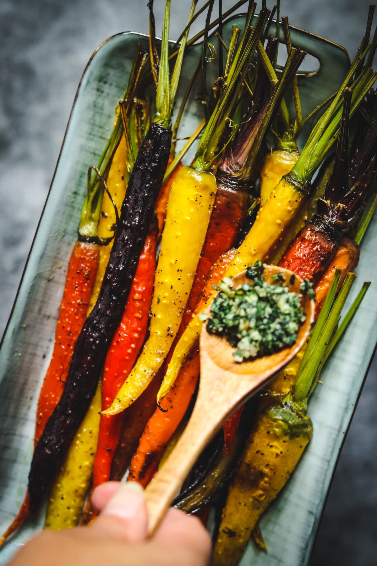 Carrot top pesto being spooned onto roasted carrots.
