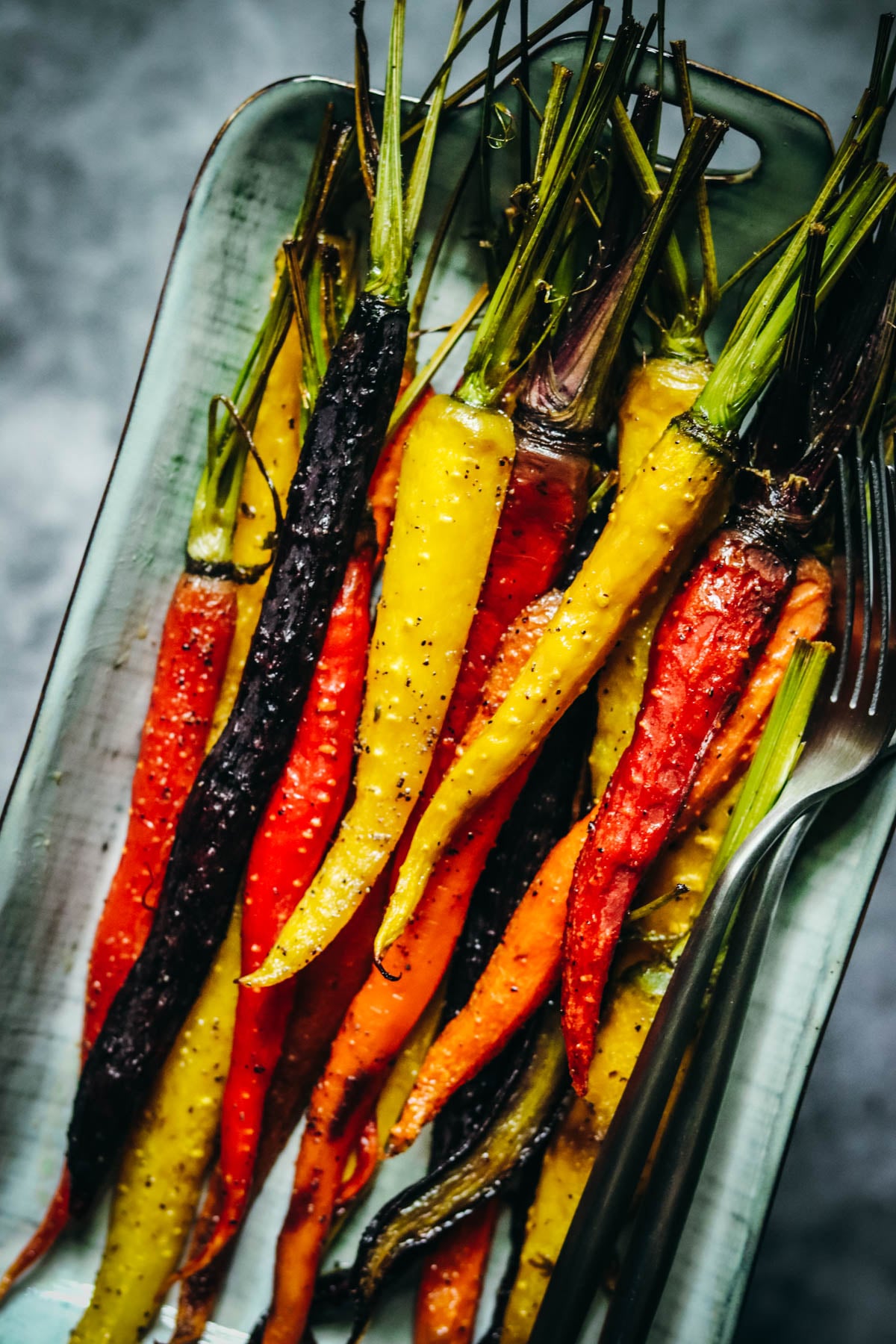 Roasted rainbow carrots and two forks in a gray dish.