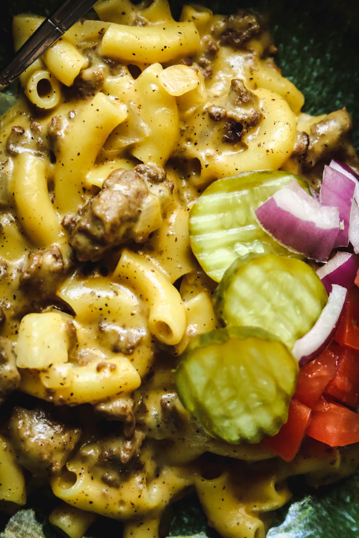 closeup photo of cheeseburger macaroni with pickles and onions.