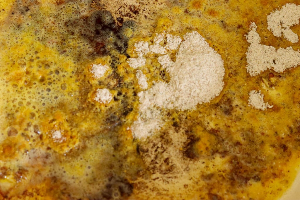 Adding reserved seasoned flour to the pan to make the sauce.