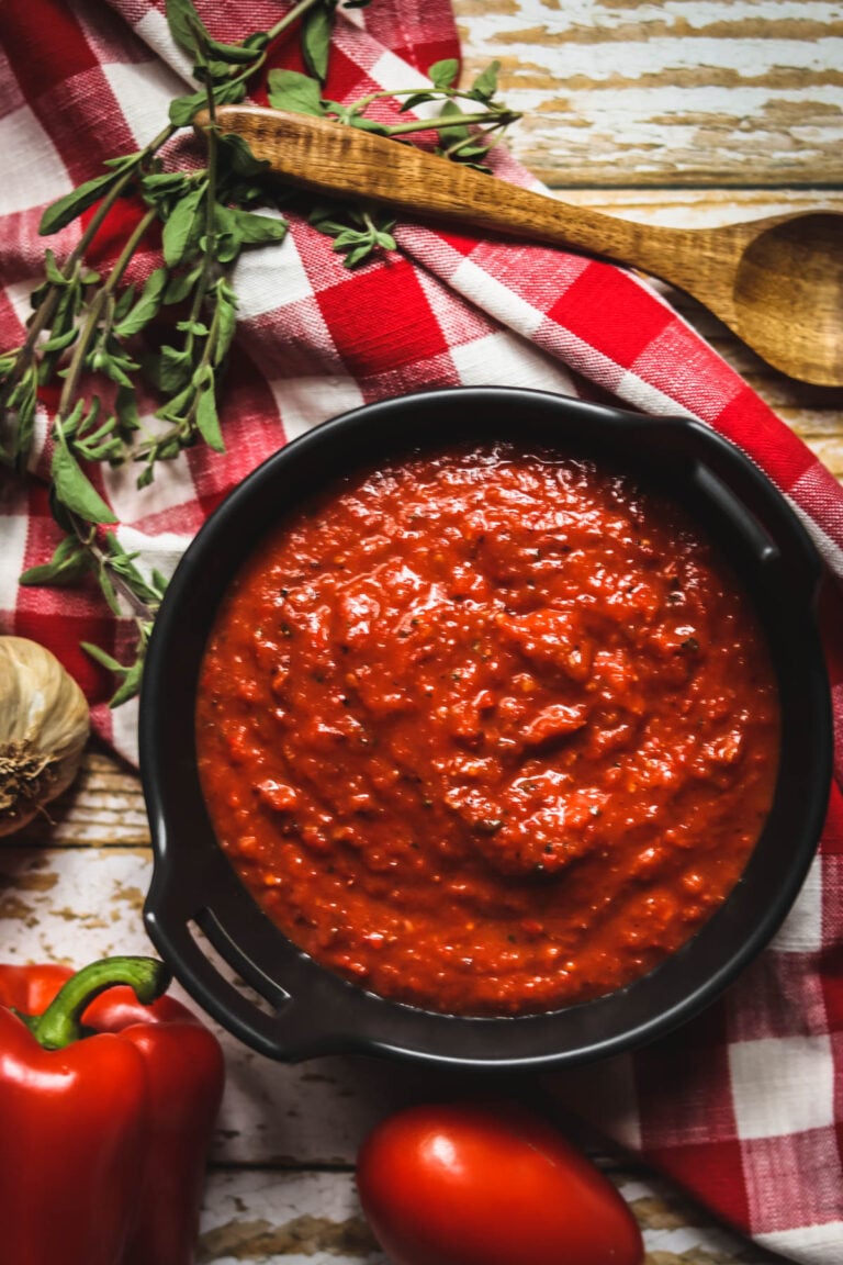 Tomato and Red Pepper sauce on a bowl next to red bell pepper, tomato, and garlic.