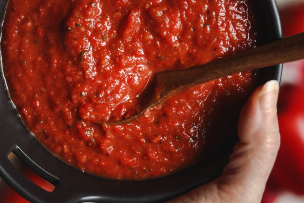 Hand holding a bowl of roasted tomato and red pepper sauce.