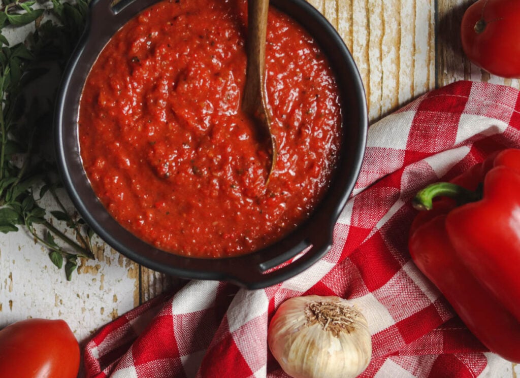 Red Pepper and Tomato Sauce in a black bowl with a wooden spoon.