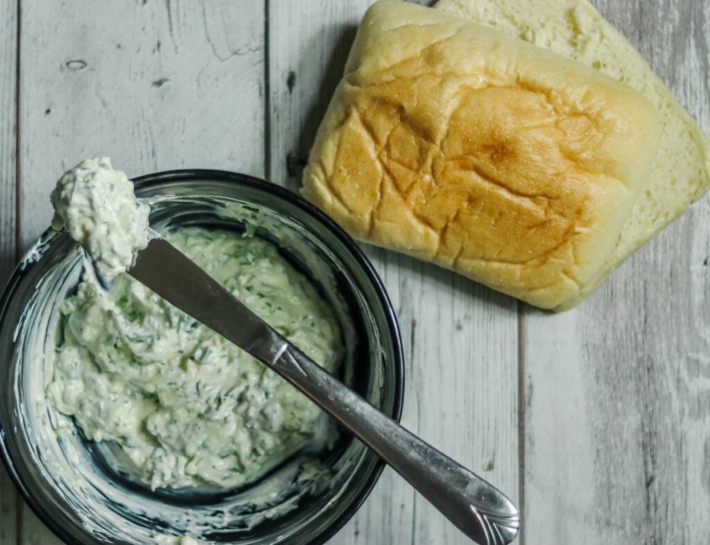 Bowl of cream cheese spread with a knife and a ciabatta roll.
