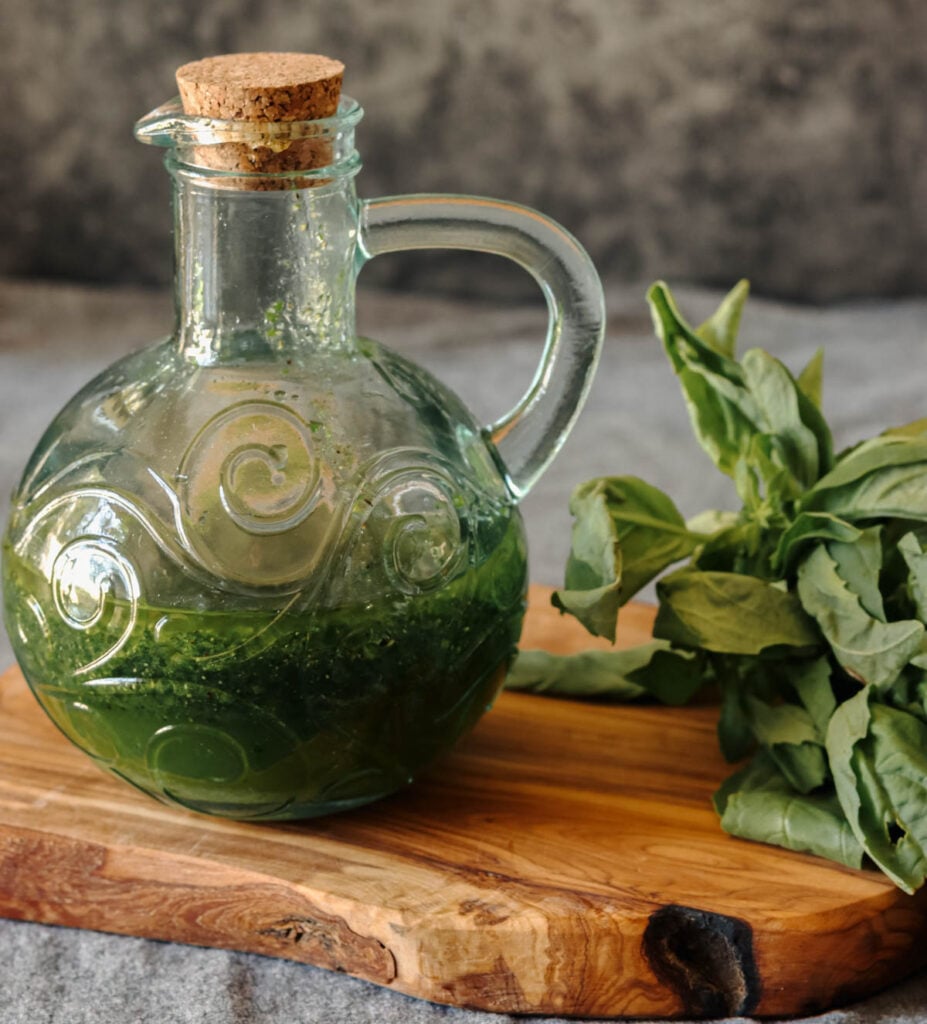 Glass bottle of fresh basil vinaigrette and fresh basil leaves.