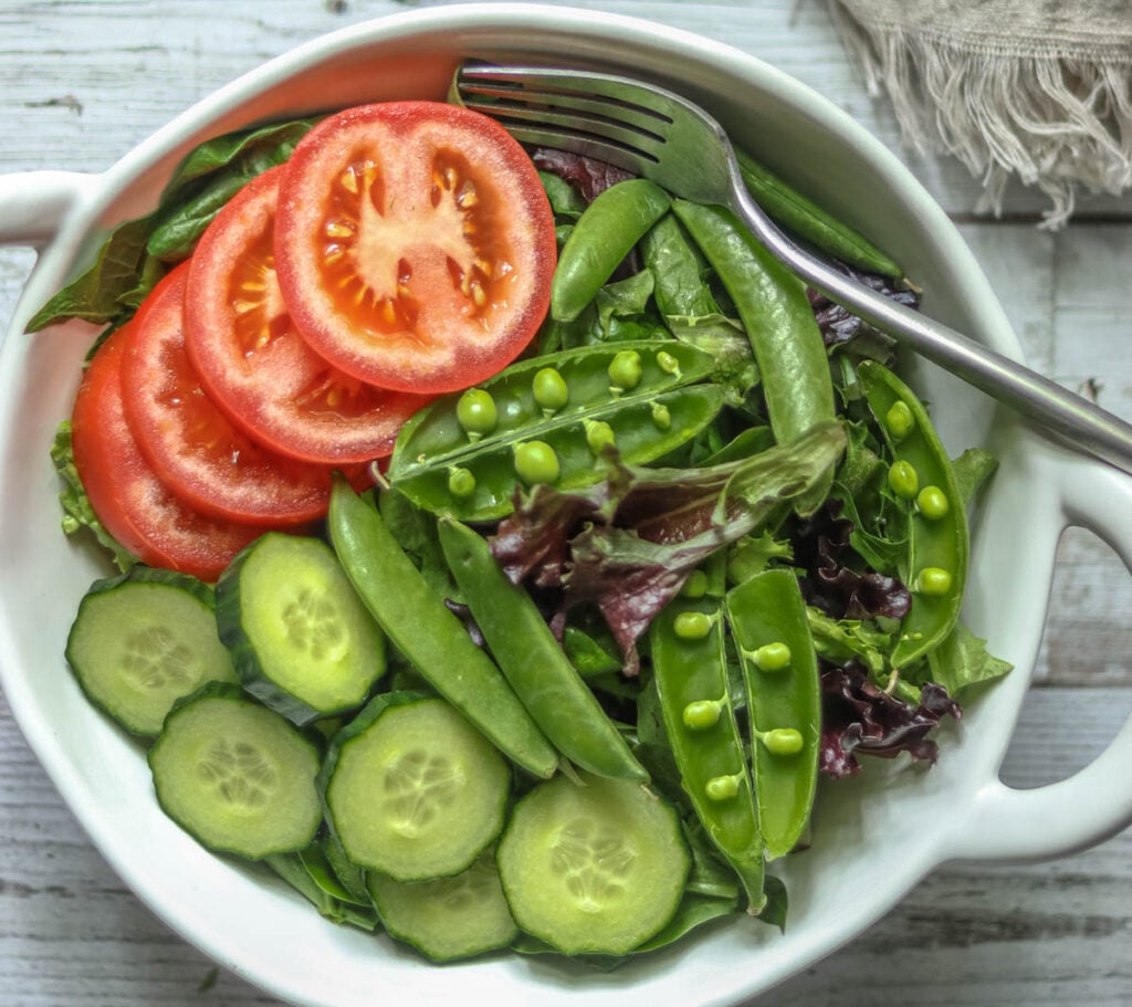 Green salad in a white bowl with a fork.