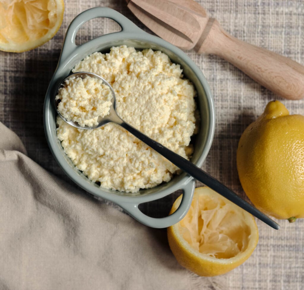 Homemade ricotta cheese with a spoon and fresh lemons.