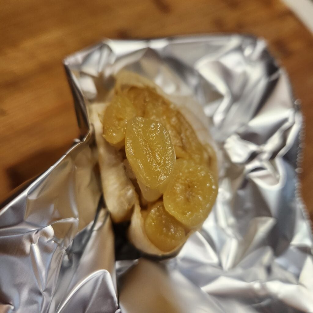 Roasted garlic cloves being squeezed from garlic skin.