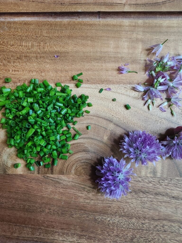 Chopped chives and chive flowers on a cutting board.