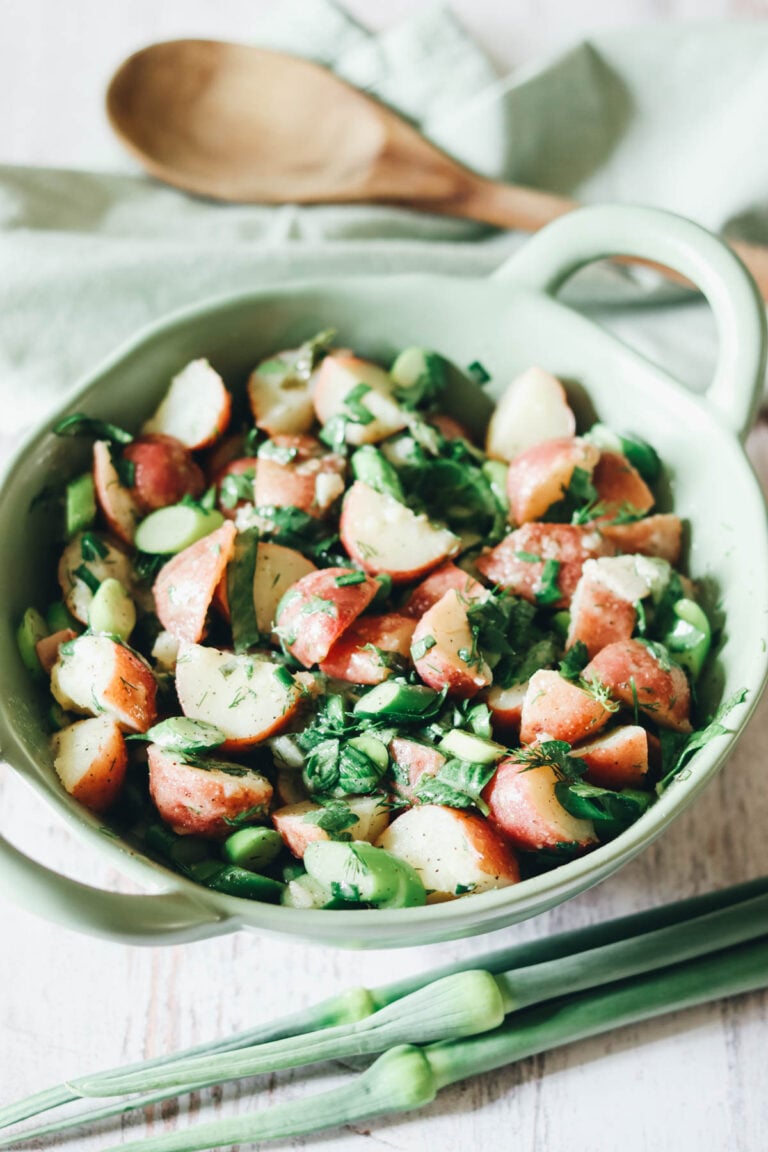Bowl of leek scape potato salad with a wooden spoon.